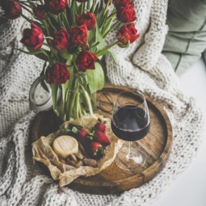 Red wine, snacks and tulips over knitted blanket, square crop